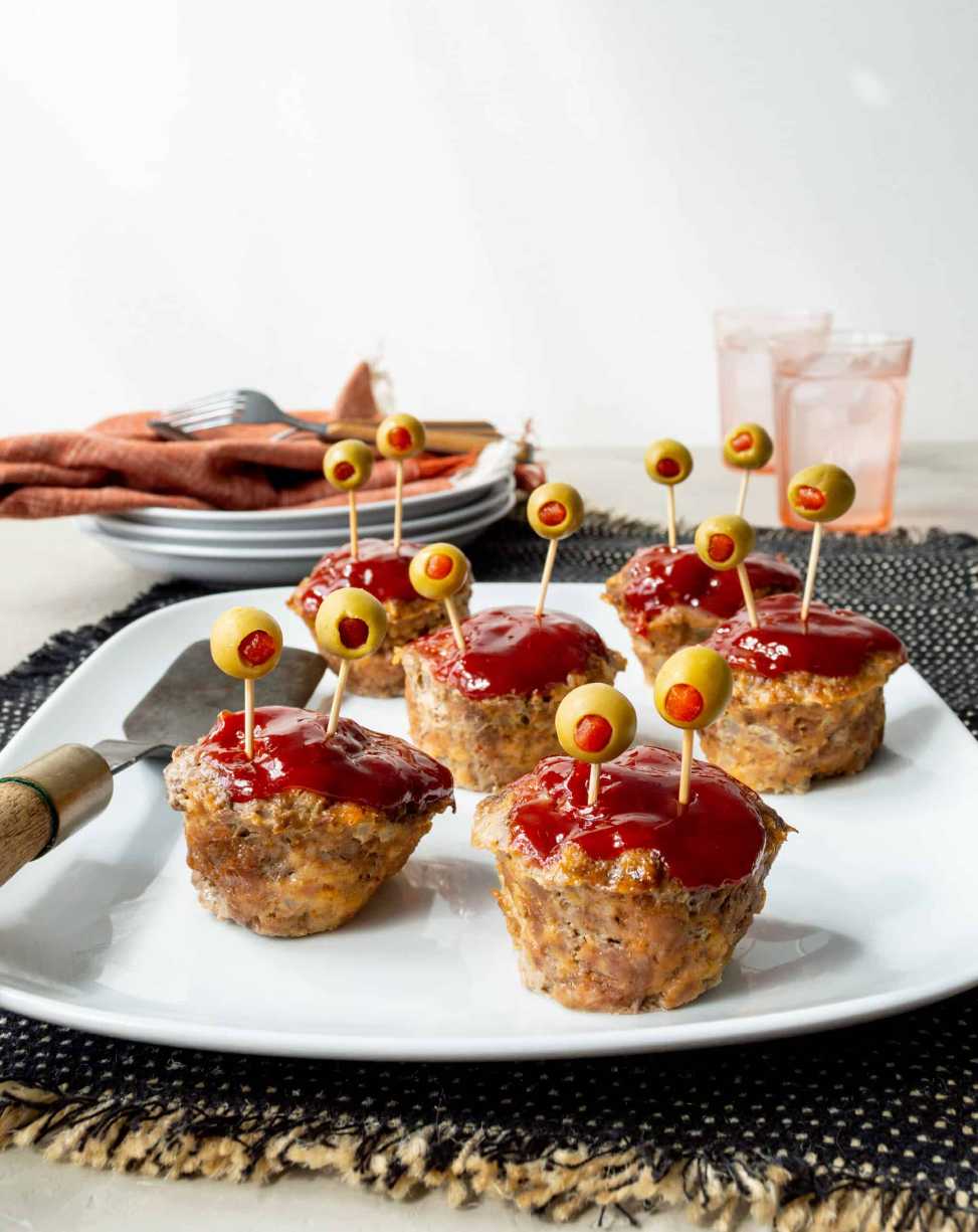 Bite‑size meatloaf rounds topped with ketchup “blood” and olive “eyes” on a spooky tray